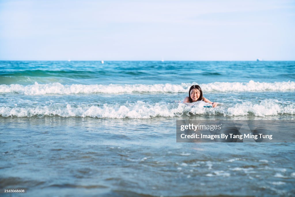 Cheerful teenage girl enjoying body boarding in sea on sunny day