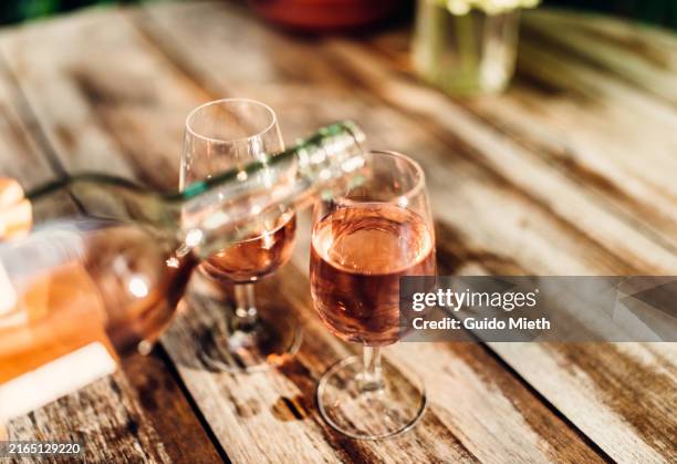 a hand pouring wine into two glasses ready to cheering and drink. - vino rosado fotografías e imágenes de stock
