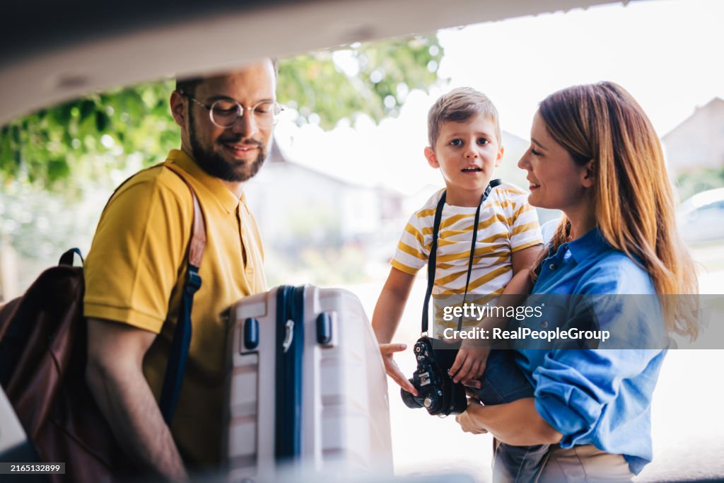 Smiling family packing car trunk with vacation luggage