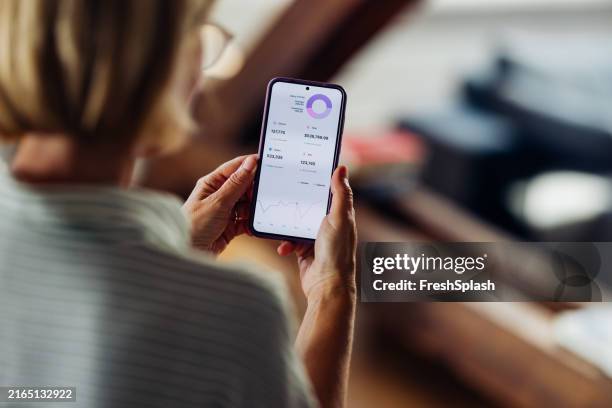 woman analyzing financial data on smartphone at home - over the shoulder view stock pictures, royalty-free photos & images