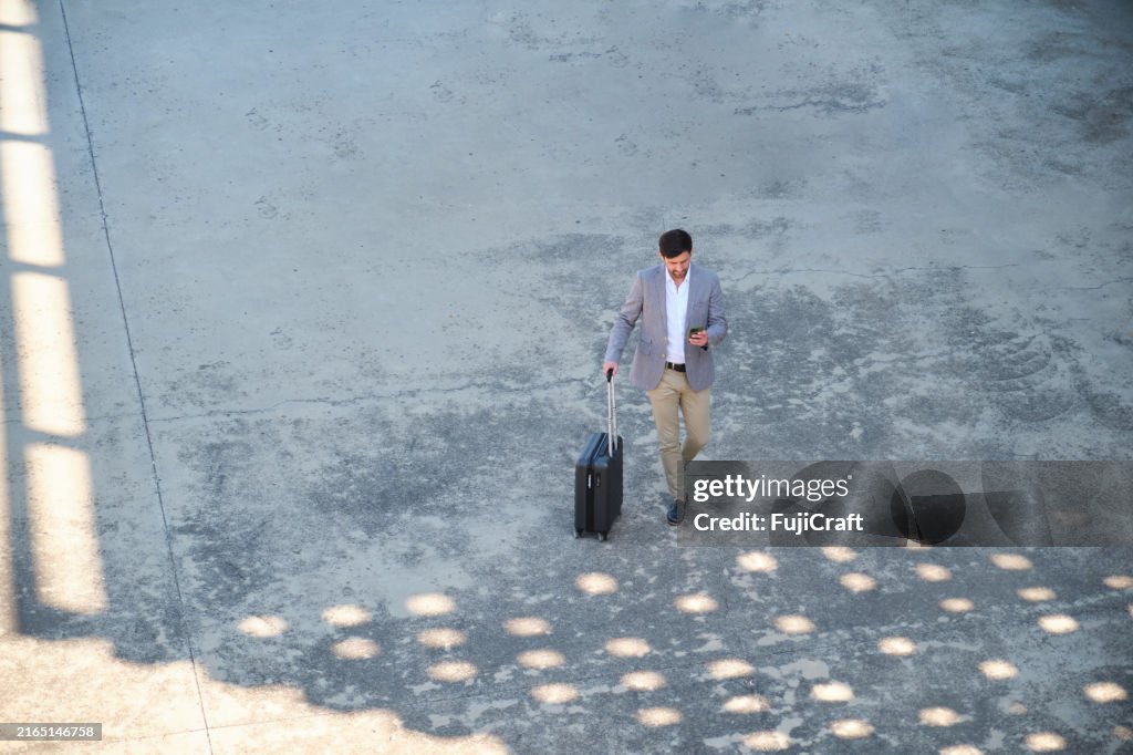 Businessman walking with suitcase using mobile phone