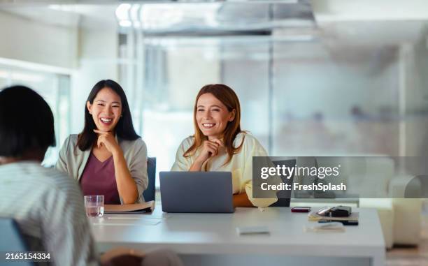 two businesswomen smiling during a meeting in modern office - japanese ethnicity working woman stock pictures, royalty-free photos & images