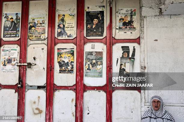 Woman sits near the entrance of a shop bearing pictures of Palestinians killed during the ongoing conflict with Israeli forces, in the Balata refugee...