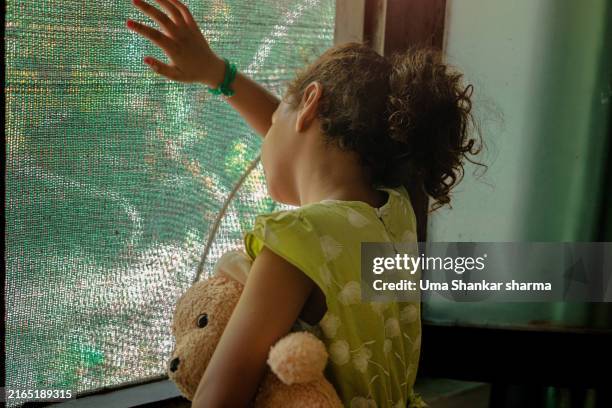 children's mental health: a young girl gazes out of a window while clutching her teddy bear. - stroke illness stock pictures, royalty-free photos & images