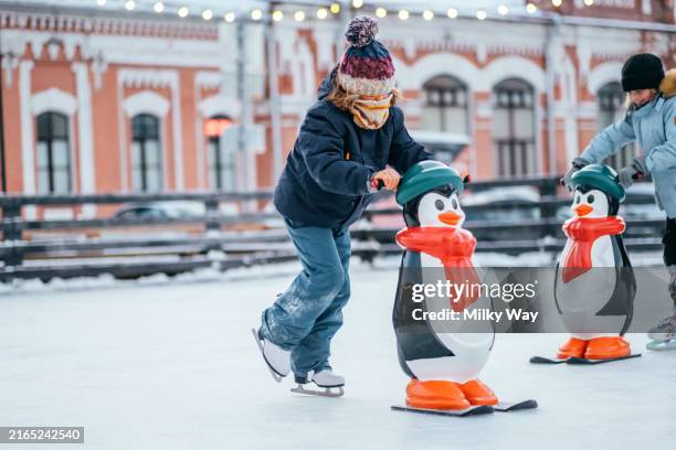 children on the ice rink, practicing ice skating, using ice pinguin figure as prop. - ice skate stock pictures, royalty-free photos & images