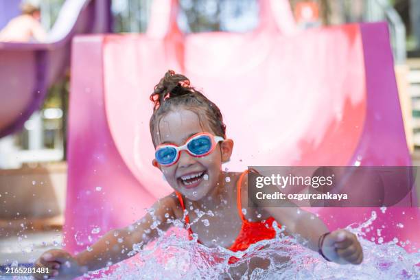 little girl playing on water slide in outdoor pool on a hot summer day - water park stock pictures, royalty-free photos & images