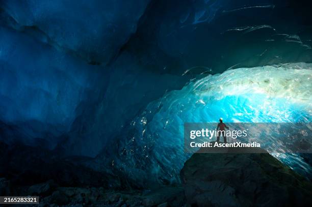 explorer stands in mouth of ice cave at night - extreme sports stock pictures, royalty-free photos & images