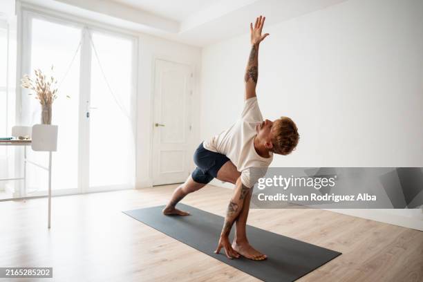 uomo che alza il braccio che pratica lo yoga con posizione triangolare a casa - metodo pilates foto e immagini stock