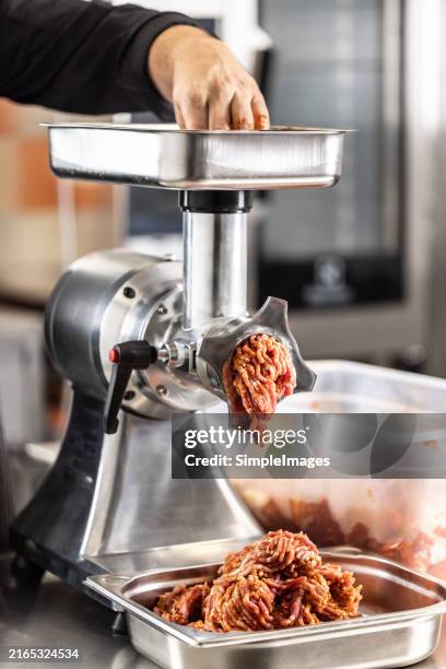 male chef butcher doing fresh ground beef for burgers in the restaurant. he put small pieces of fresh beef meat in the grinder to make ground beef - meat grinder stock pictures, royalty-free photos & images