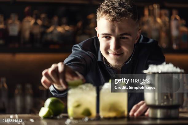 the bartender very precisely prepares the tropical caipirinha cocktail drink. he decorates the glass with a lime. - caipirinha foto e immagini stock