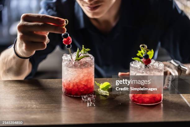 the bartender very precisely prepares the bramble cocktail drink. he decorates the glass with an mint leaves. - raspberry cocktail stock pictures, royalty-free photos & images