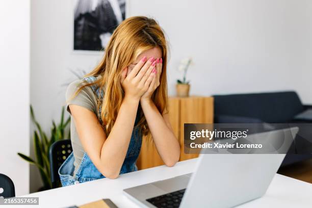 stressed young woman with hands in front of her eyes, feeling sad and depressed. she is working on laptop at home. - student behind laptop stock pictures, royalty-free photos & images