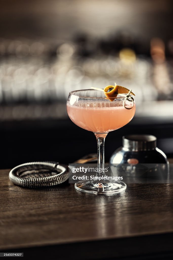 Orange alcoholic cocktail drink Cosmopolitan decorated with orange peel on bar counter.