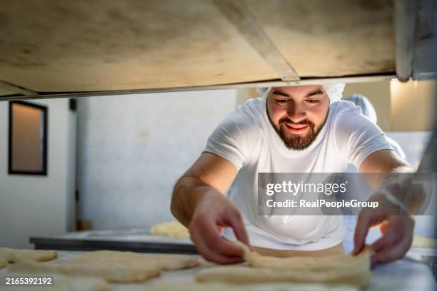baker adjusting dough pieces on a baking tray front view. - baking bread stock pictures, royalty-free photos & images