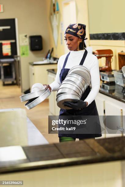 woman working in bakery kitchen moves stack of cake pans - baking pan stock pictures, royalty-free photos & images