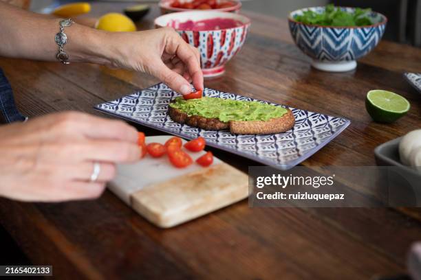 Closeup Of A Womans Hands Preparing A Toast With Avocado Cherry Tomatoes And Red Onion High-Res Stock Photo