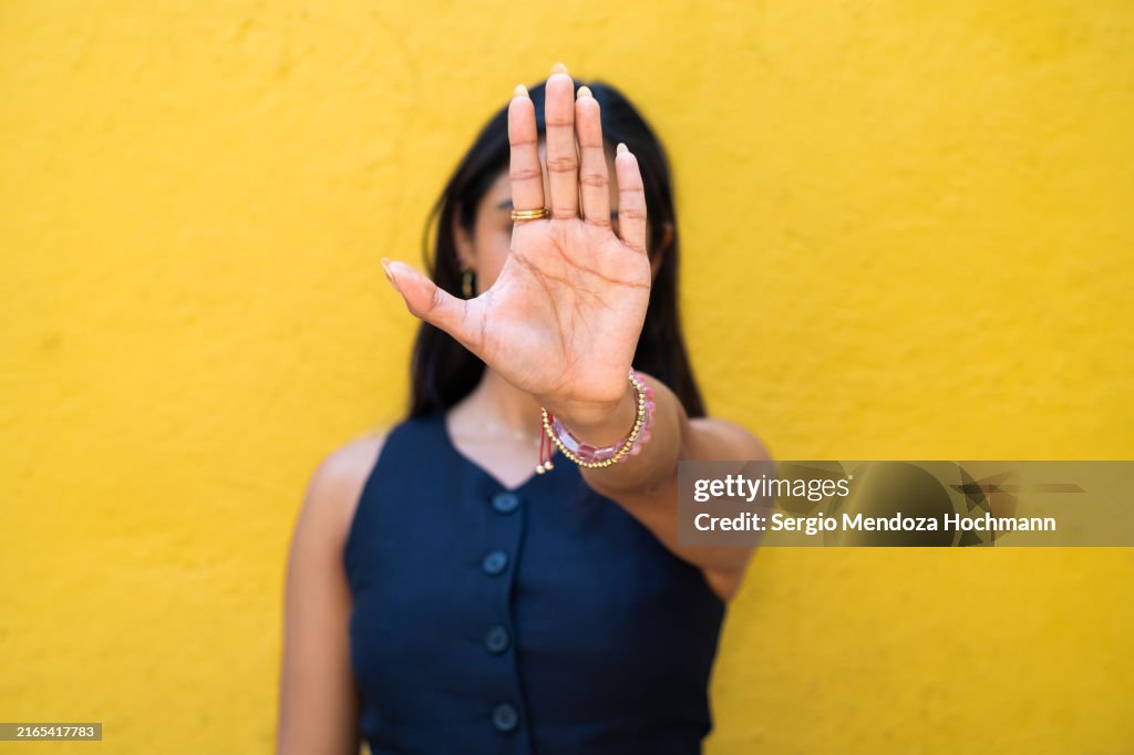 Latino woman looking at the camera and gesturing to STOP, hand obscuring her face