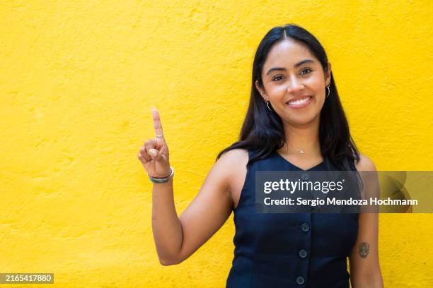 latino woman smiling, looking at the camera and giving the number one sign - number one finger sign stock pictures, royalty-free photos & images