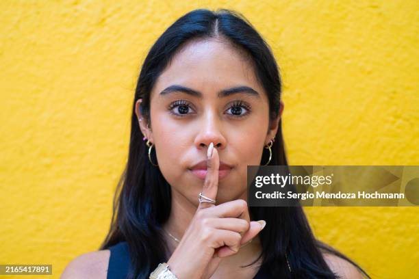 latino woman looking at the camera with a finger on her lips, asking for quiet, silence - woman with finger on lips stock pictures, royalty-free photos & images