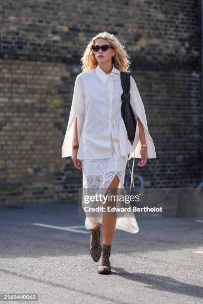Guest wears black sunglasses, gold hoop earrings, white button up tied long sleeve with slits shirt, black Bottega Veneta leather bag, gold...