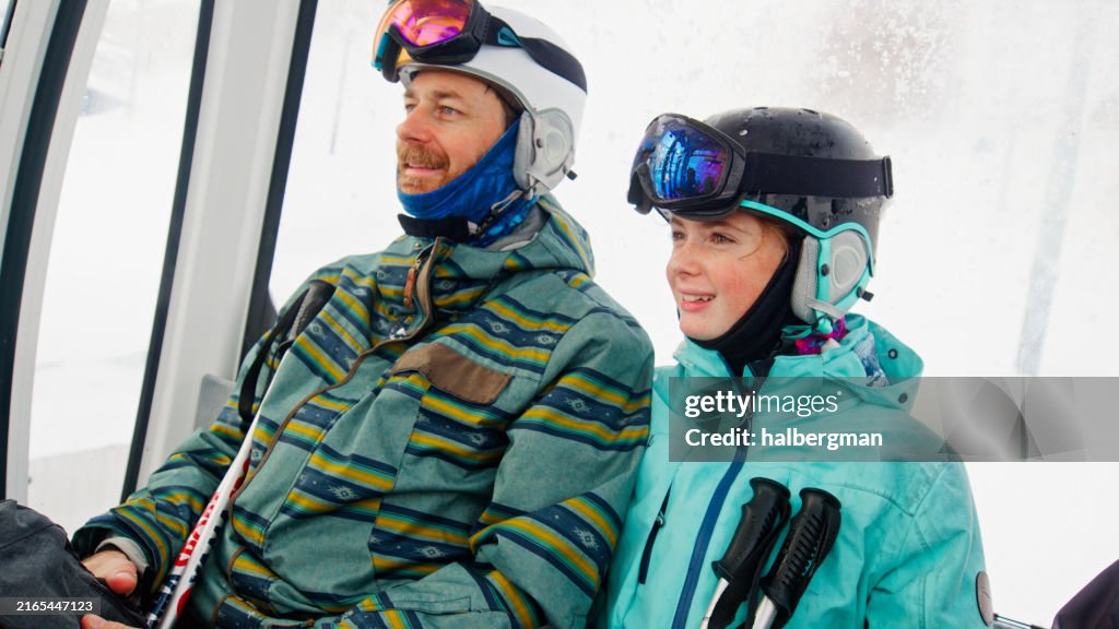 Middle Aged Man Sitting with Teenage Daughter In Ski Gondola