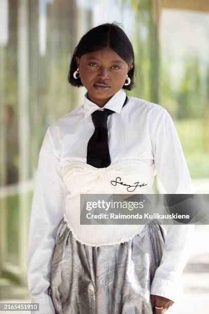 Guest wears long silver or grey skirt, white shirt, black tie, white corset and black bag outside OpéraSport show during the Copenhagen Fashion Week...