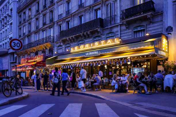 August 2024, France, Paris: Olympia, Paris 2024: Passers-by walk past the restaurants "Le Cristal Bar Brasserie" and "Brasserie Nai" in the evening....