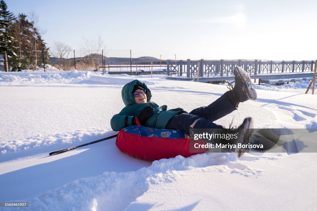Winter fun on a snowy mountain. The boy is rolling down the snowy mountain on the snow tube.