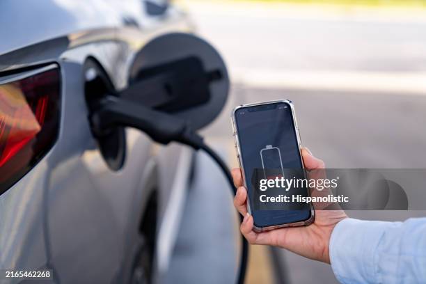 primo piano su una donna che ricarica la sua auto elettrica e utilizza un'app mobile - basso posizione descrittiva foto e immagini stock