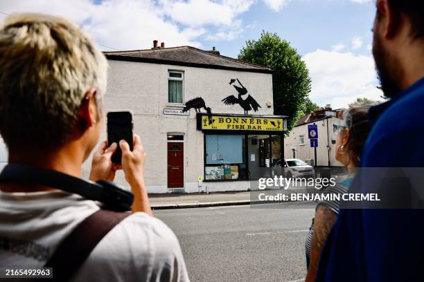 People gather to look at an artwork by street artist Banksy, the fifth to be released this week, depicting two pelicans catching fish, painted on top...