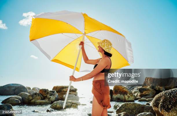 giovane donna sorridente che mette su un ombrellone su una spiaggia in estate - ombrellone da spiaggia foto e immagini stock