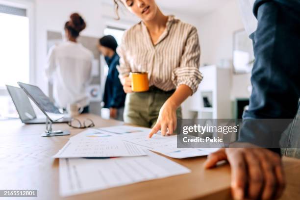 compañeros jóvenes repasando el papeleo en la oficina - trabajo de oficina fotografías e imágenes de stock