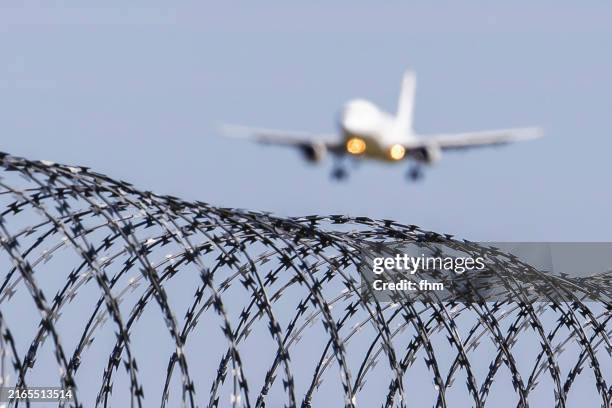 barbed wire with approaching passenger aircraft in the sky - zaun stock-fotos und bilder