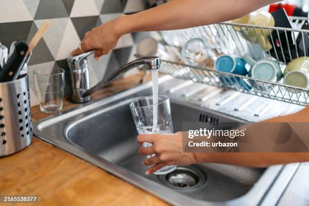 mujer joven llenando un vaso de agua en el fregadero - grifo herramientas profesionales fotografías e imágenes de stock