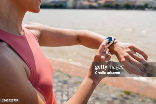 young woman checking fitness activity on a smartwatch after running on the quayside in budapest in hungary - fitness tracker stock pictures, royalty-free photos & images
