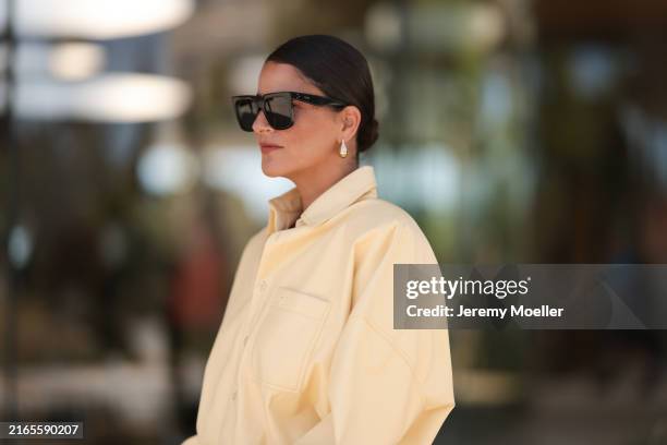 Fashion week guest is seen wearing an oversized yellow blouse with collar and long sleeves, a yellow pleated skirt, high blue sandals, black...
