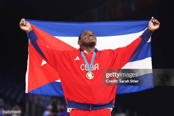 Gold medallist Mijain Lopez Nunez of Team Cuba celebrates with the Cuban flag and his fifth Olympic Gold Medal on the podium after the Wrestling...