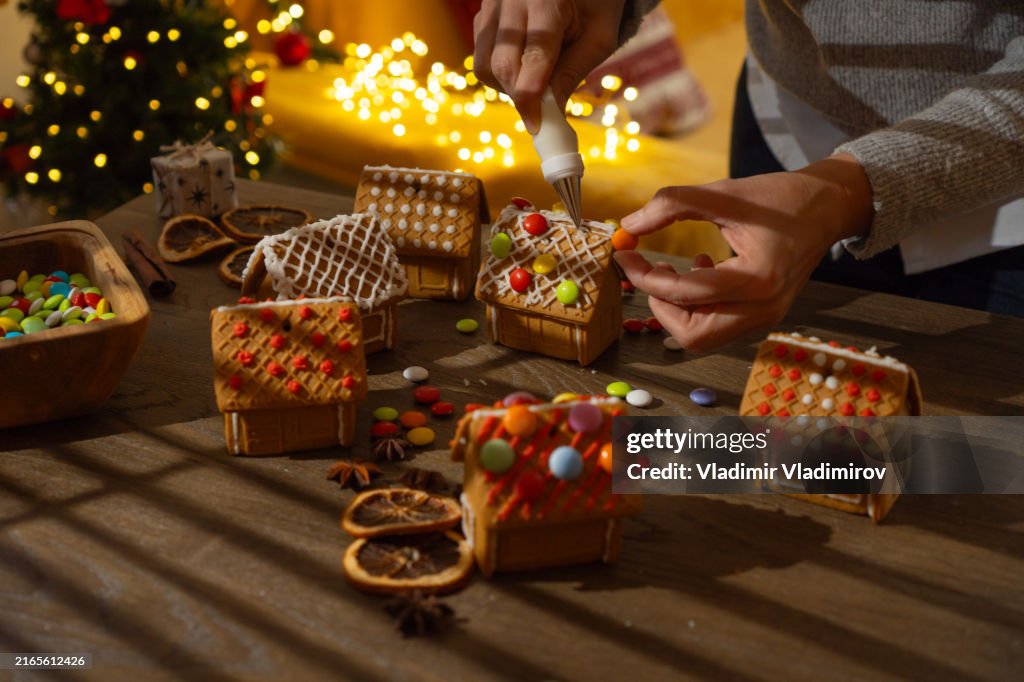 Woman is decorating small gingebread houses with candies