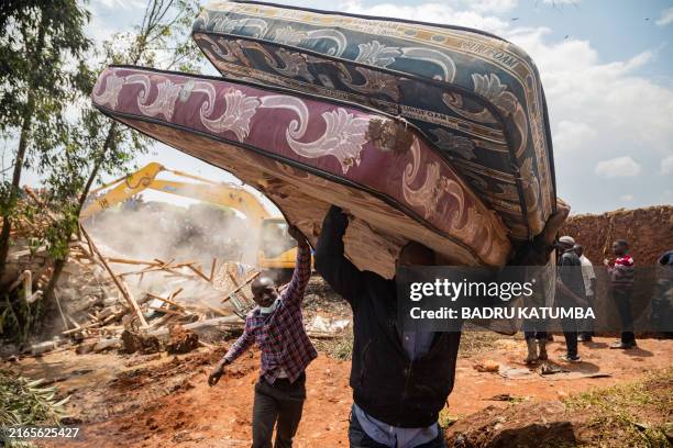 Two men carry mattresses after a landfill collapsed in Kampala on August 10, 2024. Eight people including two children were killed when a landfill in...