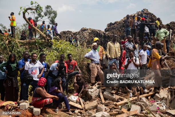 People look on as an excavator helps search for people trapped under debris after a landfill collapsed in Kampala on August 10, 2024. Eight people...
