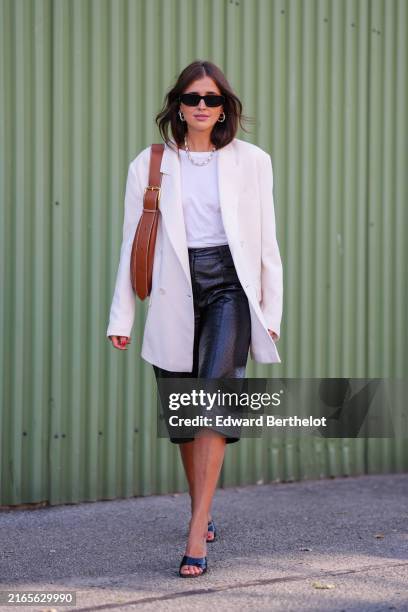 Darja Barannik wears. Black sunglasses, white necklace, white t-shirt, cream oversized blazer jacket, light brown leather bag, shiny black leather...
