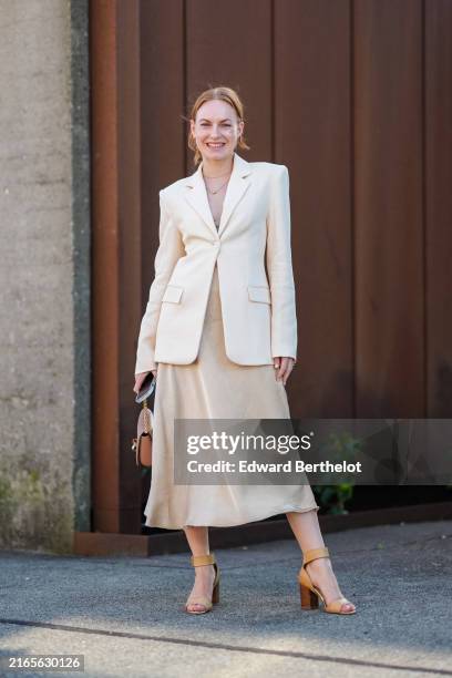 Guest wears gold hoop earrings, silver necklace, cream tailored blazer jacket, beige midi skirt, shiny light brown leather bag, light brown yellow...