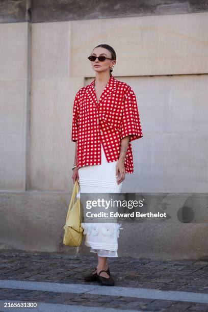 Guest wears black sunglasses, gold earrings, white and red pattern button up short sleeve shirt, silver bracelet, light yellow leather bag, white...
