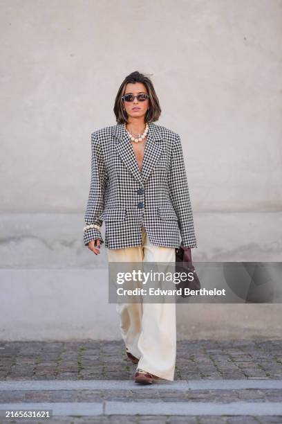 Guest wears black sunglasses, silver necklace, white beaded necklace, black and white pattern oversized blazer jacket, silver rings, white pearl...