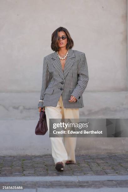 Guest wears black sunglasses, silver necklace, white beaded necklace, black and white pattern oversized blazer jacket, silver rings, white pearl...