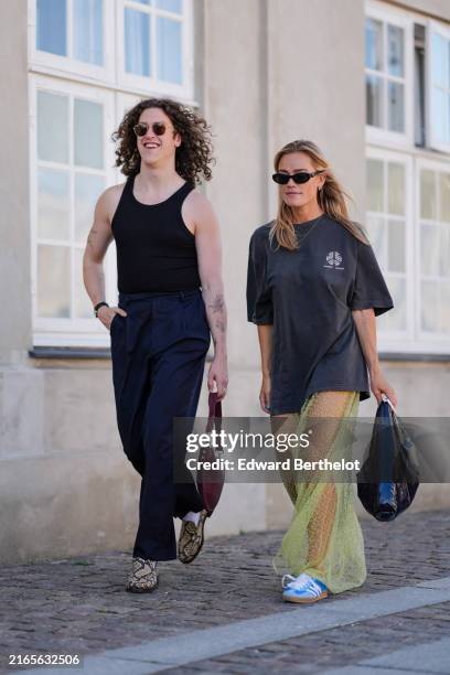 Pim Spoor wears black sunglasses black tank top, black straight pants, a watch, shiny red leather bag, white socks, brown and black animal print...