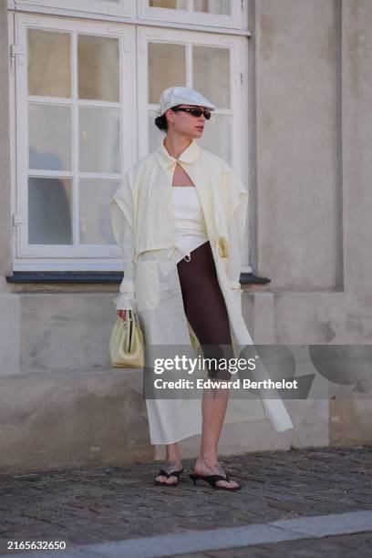 Guest wears white hat, black sunglasses, silver earrings, white bodysuit, pastel yellow windbreaker trench coat, pastel yellow leather handbag, dark...