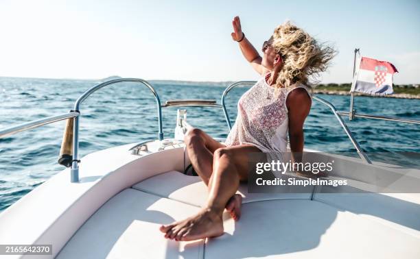 a young woman enjoying a vacation by the sea sits on the front deck of a boat in a dress and observes the horizon in the adriatic sea of the mediterranean sea. - proa fotografías e imágenes de stock