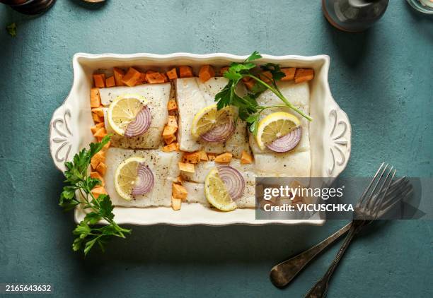 cod fish pieces in casserole pan with lemon and fresh herbs on blue  table - dorsch stock-fotos und bilder