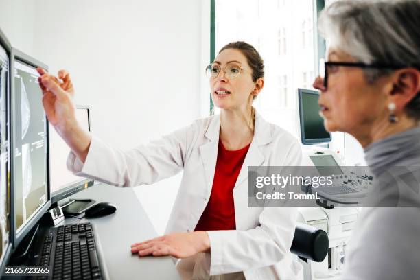 junge ärztin, die auf den computerbildschirm zeigt, während sie einem älteren patienten erklärt - old monitor computer stock-fotos und bilder